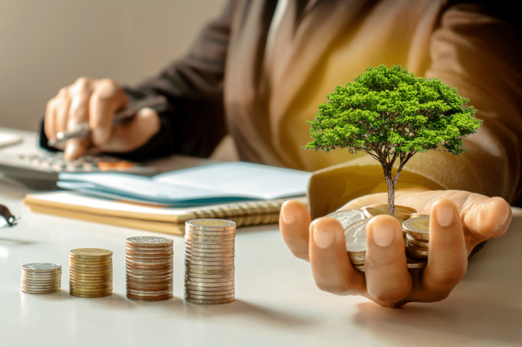 Varias columnas de monedas en una mesa y una mano sujetando un árbol simbolizando los fondos de inversión.